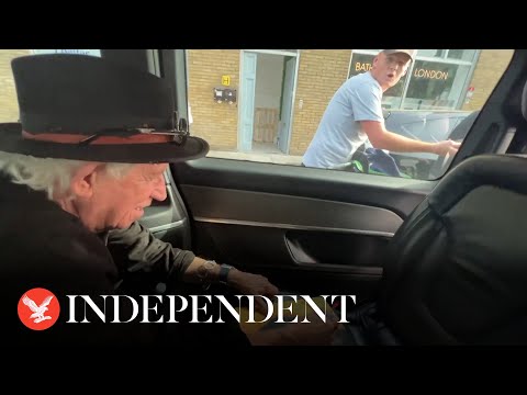 Keith Richards jokes with cyclists as he signs autograph for him in back of taxi