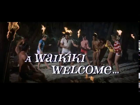 Mid-trailer frame of Elvis Presley performing with dancers in Blue Hawaii