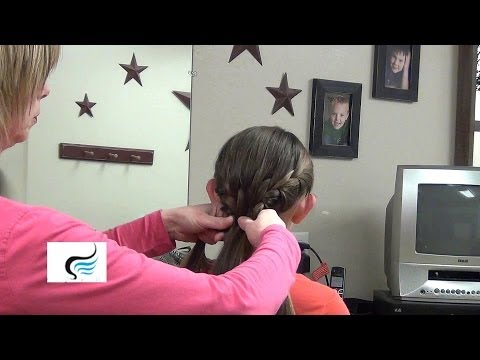 Woman demonstrating double French braid hairstyle on a child in a salon setting, with decorative stars on the wall and a television in the background.