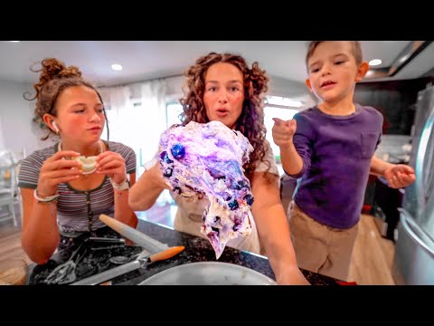 Three people gather around a kitchen counter, holding a colorful purple-blue ice sculpture head they made together.