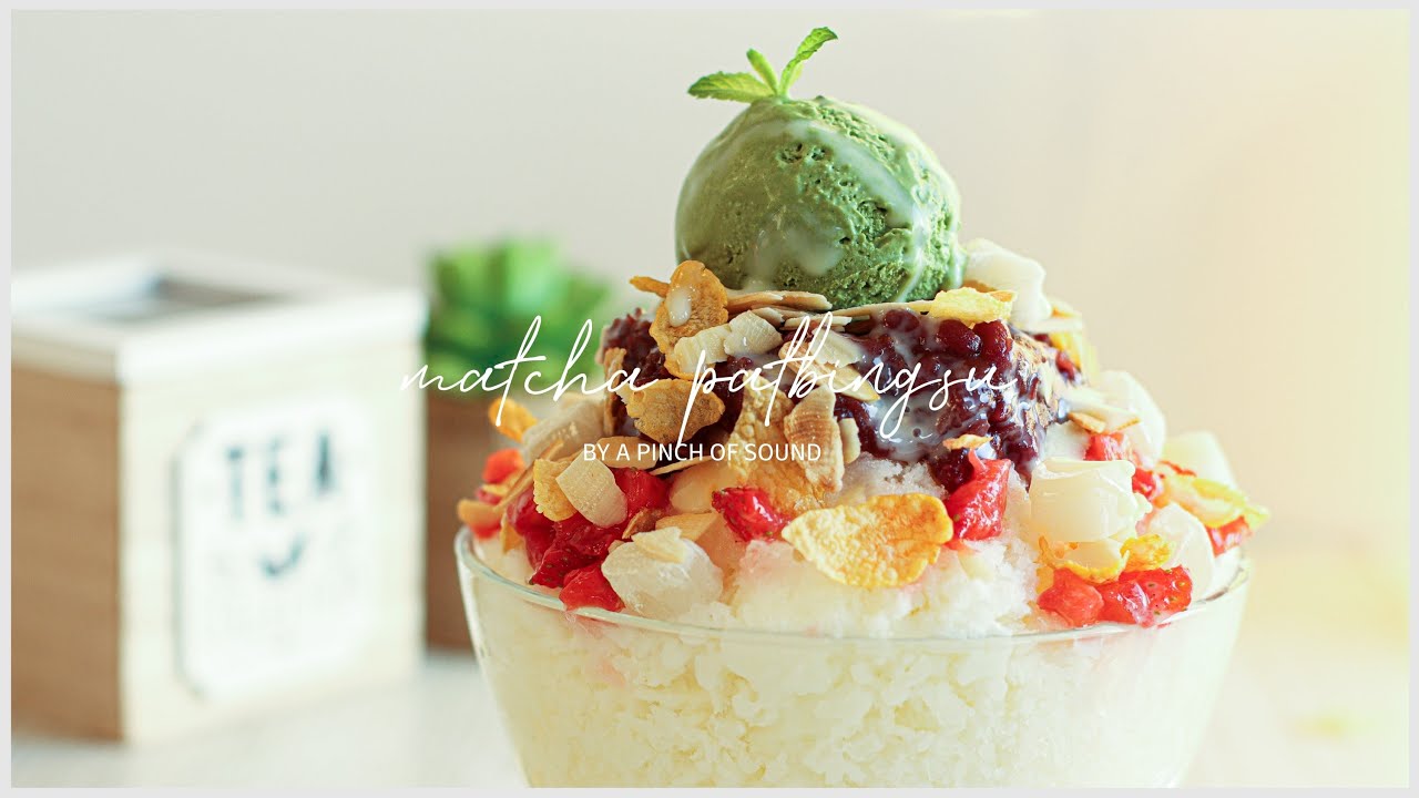 A large Korean cafe style patbingsu shaved ice dessert with a mountain of red beans condensed milk and mochi rice cake balls on top in a glass bowl