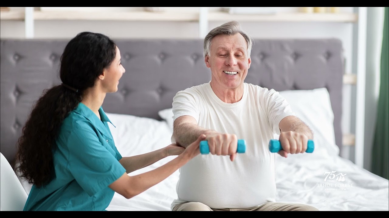 Physical therapist helping an older man lift weights in a bedroom