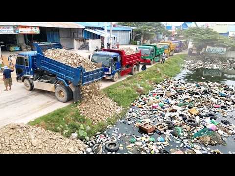 Excellent action of a dump truck unloading rocks into a canal with sewage waste, bulldozer pushing