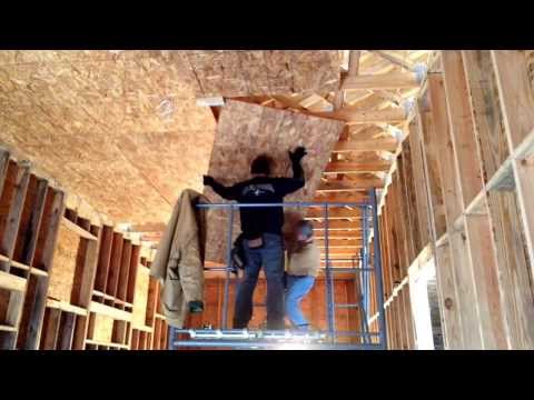 Hanging OSB plywood on a high ceiling a scaffold and two people.