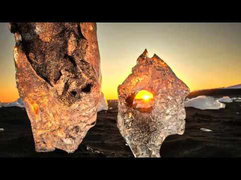 Photograph of two chunks of glacial ice at sunset, with the sun glowing through the gap between them.