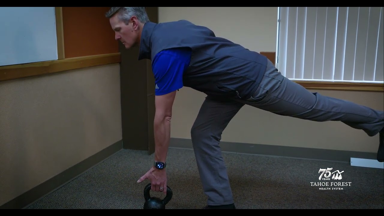 Man demonstrating an exercise stretch while holding a kettlebell weight 