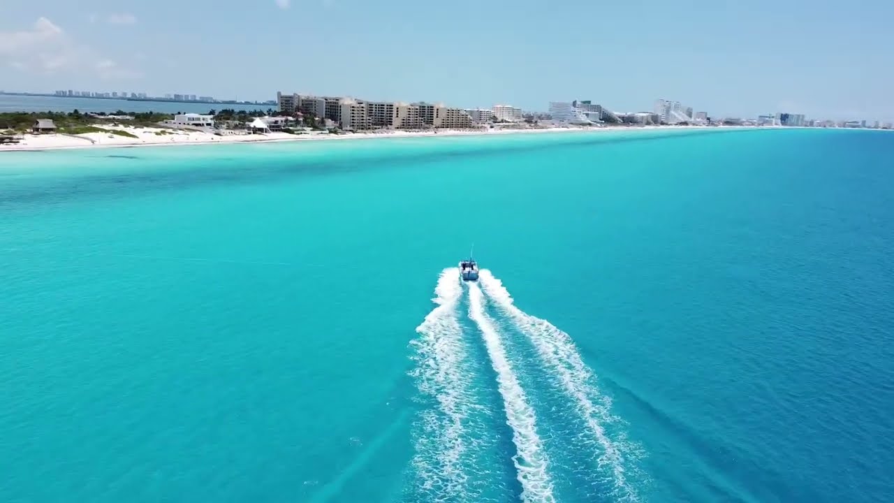 Aerial drone view over turquoise water toward the Cancun Hotel Zone shoreline