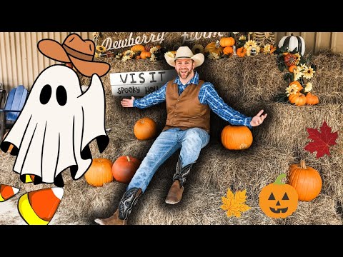 Smiling man in a cowboy outfit sits on hay bales with pumpkins and autumn decor around him, Halloween vibe.