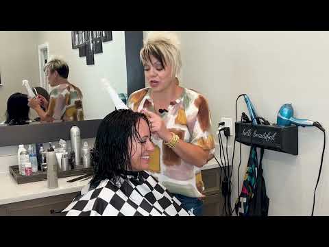 Hair stylist applying a haircut to a woman in a salon, featuring a checkered cape and various hair products, emphasizing age-appropriate styling for women over 40.