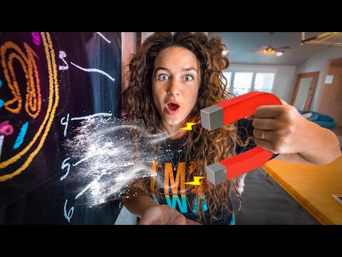 Woman with a red horseshoe magnet sprays chalk dust from a chalkboard in a science demonstration, eyes wide with surprise.