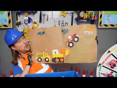 Man in a blue hard hat and orange safety vest holds up a cardboard craft featuring a yellow dump truck, a yellow excavator, and a red monster truck climbing a grassy hill in a workshop setting.