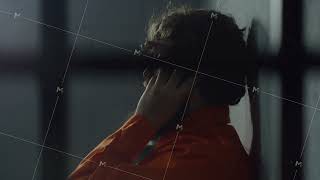 Criminal in orange uniform talks on phone in prison cell