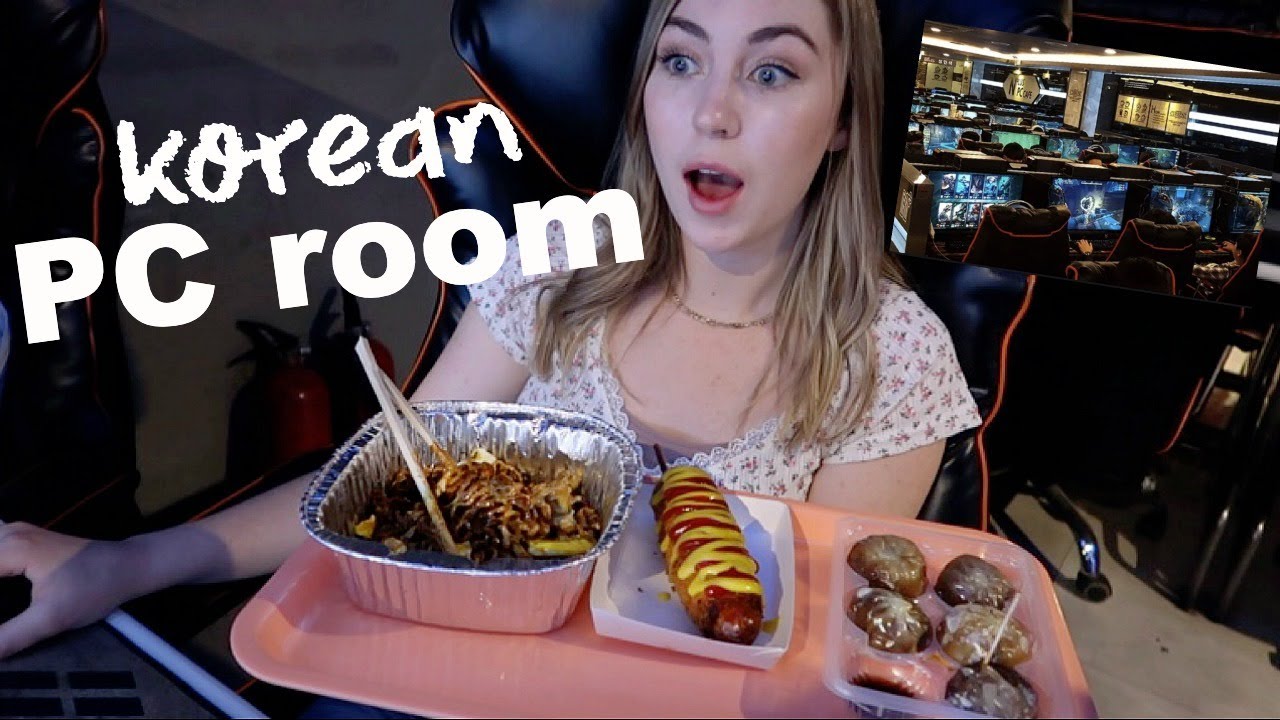 A first time visitor eating Korean ramyeon and snacks at a PC bang gaming station while playing on a curved monitor