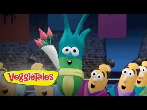 Green veggie character holding a bouquet of pink roses on stage, VeggieTales logo visible in foreground, smiling audience of veggies nearby.