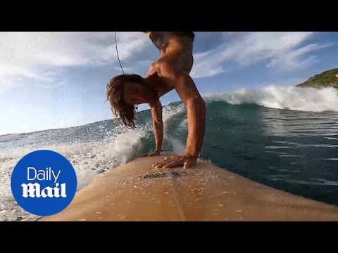 Daredevil surfer performs headstand whilst riding waves