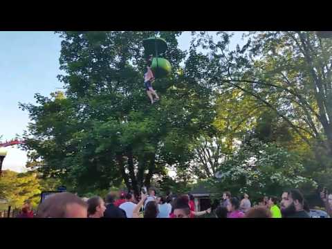 Crowd Gathers Beneath A Girl Dangling From An Amusement Park Ride To Catch Her When She Falls