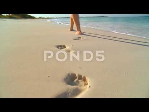 Young caucasian girl leaving footprints in the white sand of a tropical beach