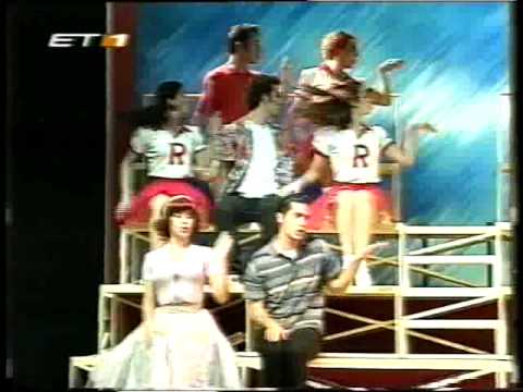 Το χορευτικό νούμερο “We Go Together” [«Πάμε παρέα»] από το Grease: Το πάρτυ αρχίζει…, θέατρο Βέμπο, Αθήνα, 1997, σε σκηνοθεσία David Gilmore [Ντέηβιντ Γκίλμορ] και μετάφραση Έλενας Ακρίτα, με τον Μάριο Φραγκούλη και τη Μαρία Λουίζα Βασιλοπούλου στους κεντρικούς ρόλους. Στο τελικό σύνολο ο θίασος συγκεντρώνεται σε πολυεπίπεδη διάταξη πάνω στις μεταλλικές σκαλωσιές και τραγουδά εν κινήσει, όπως απαιτεί η «τριπλή απειλή». Η παραγωγή ανήκει στις αδειοδοτημένες μεταφορές διεθνών τίτλων, και τα σκηνικά και τα κοστούμια του Terry Parsons [Τέρρυ Πάρσονς] αναπαράγουν το πρωτότυπο σχέδιο.