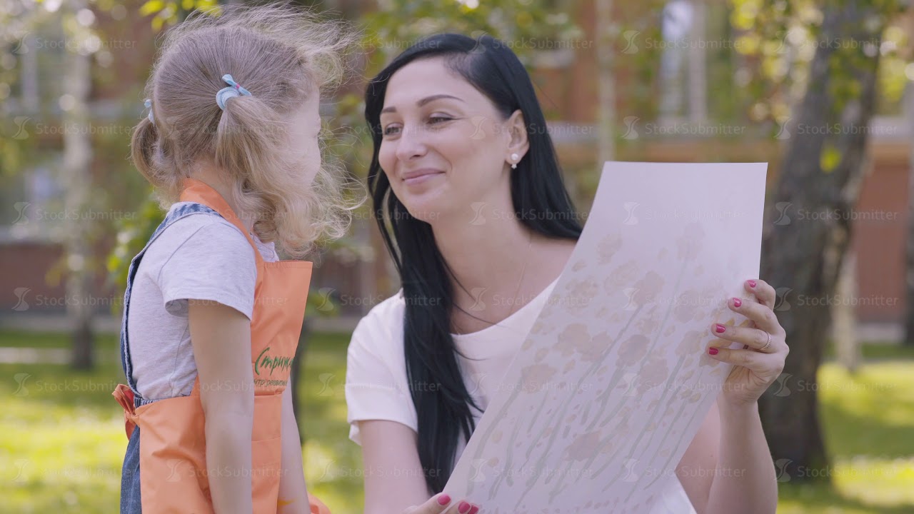 Baby gives mother a picture drawn in kindergarten, mom kisses daughte