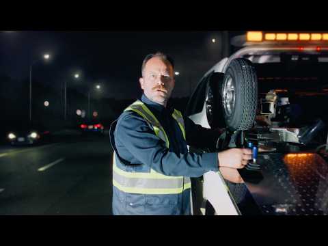 A stopped CAA tow truck with amber lights flashing helps a member on the side of the road. A vehicle passing the scene slows down and moves over.