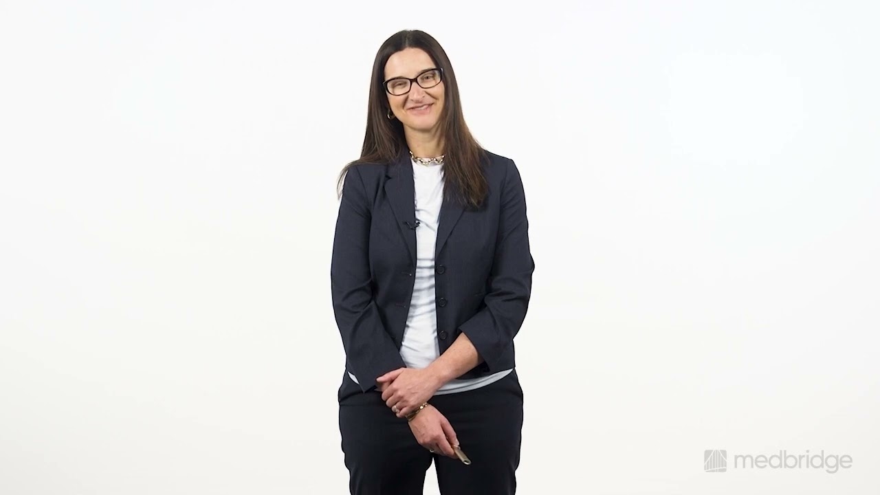 A professional woman in glasses and a dark blazer stands with hands folded, suitable for medbridge healthcare training.