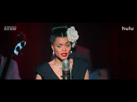 Trailer frame: Holiday on a grand stage, orchestra behind, as camera booms over a cheering audience