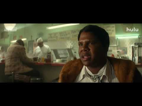 Official trailer still: Andra Day as Billie Holiday under a spotlight with a big-band behind her