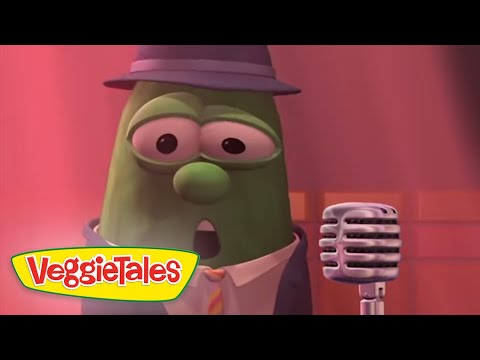 Green VeggieTales character in a hat and tie singing into a vintage microphone on a pink stage with VeggieTales branding nearby.