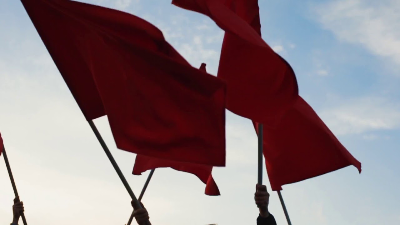 hands of a group of people waving red flags against blue sky