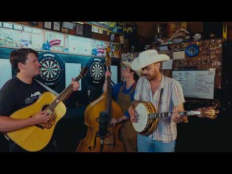 A live band playing banjo, guitar, and upright bass in front of the dartboards during a real Villager People Podcast episode