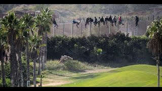 Desperate Moroccans sit on top of border fence beside luxury golf