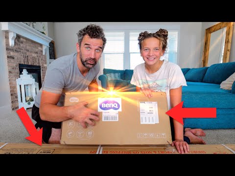 Man and girl unboxing a BenQ package on a living room floor, delighted by the reveal.