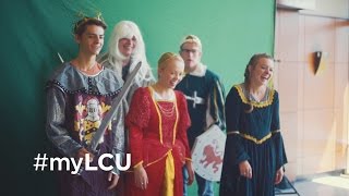 A group of five students standing in front of a greenscreen placed in the Moddy Auditorium Lobby in medieval costumes, laughing and having fun with #myLCU in transparent white letters in the bottom left-hand corner