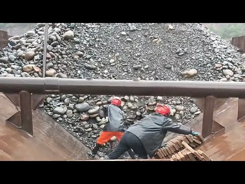 Barge unloads large river rocks in the rain - workers must wear raincoats and helmets to work