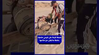 مسنة فلسطينية تتنقل على كرسي متحرك حاملة ما تبقى من متاعها بينما يمدّ لها الشباب يد العون على الطريق thumbnail