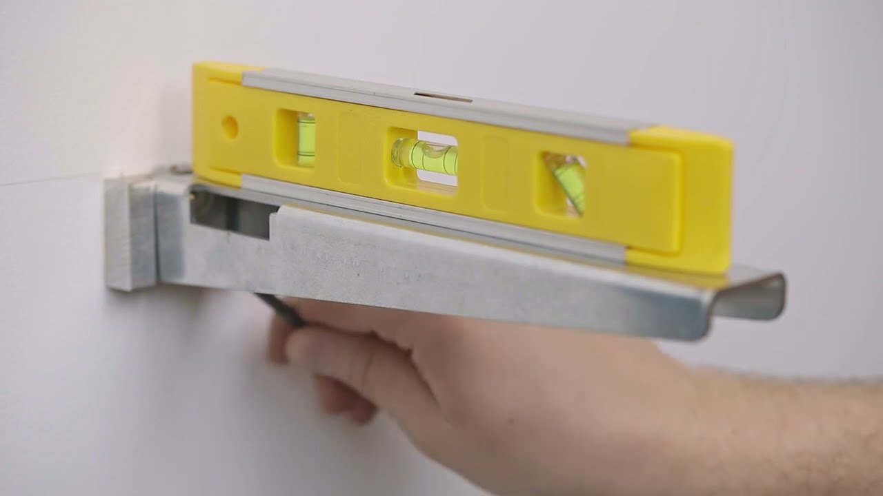 Torpedo level resting on a wall-mounted T-LOC steel bracket mid-install