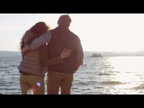 Back view of romantic couple hugging and watching sunset on lake shore