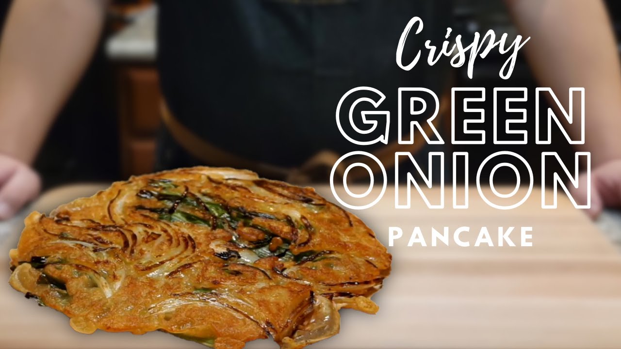 Crispy golden brown pajeon Korean scallion pancake being cut into pieces on a wooden board