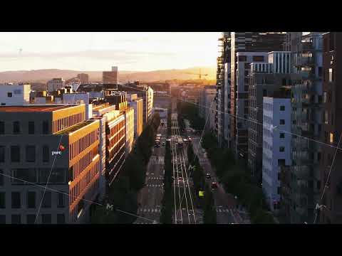 Apartment buildings along wide street with tram line. Forwards fly above boulevard at sunset. Oslo