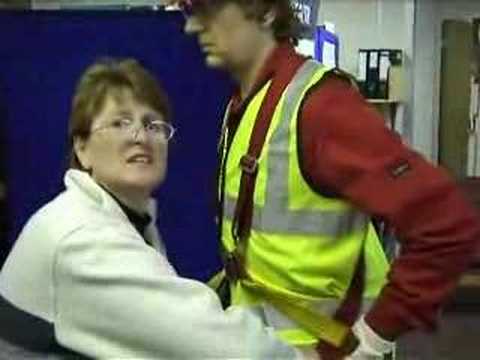 mannequin-man performming as a Living Mannequin: Fall arrest harness being put onto mannequin man by member of the public at a Safety clothing and PPE exhibition by ARCO at family open day at BAE (British Aerospace Engineering) systems in Rochester #5 (flash) for Arco on 06/07/2002