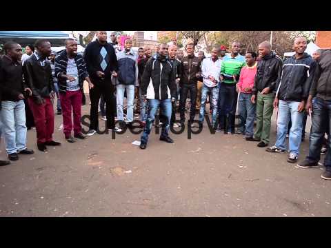 Extreme long shot. A male choir sings as people gather to...