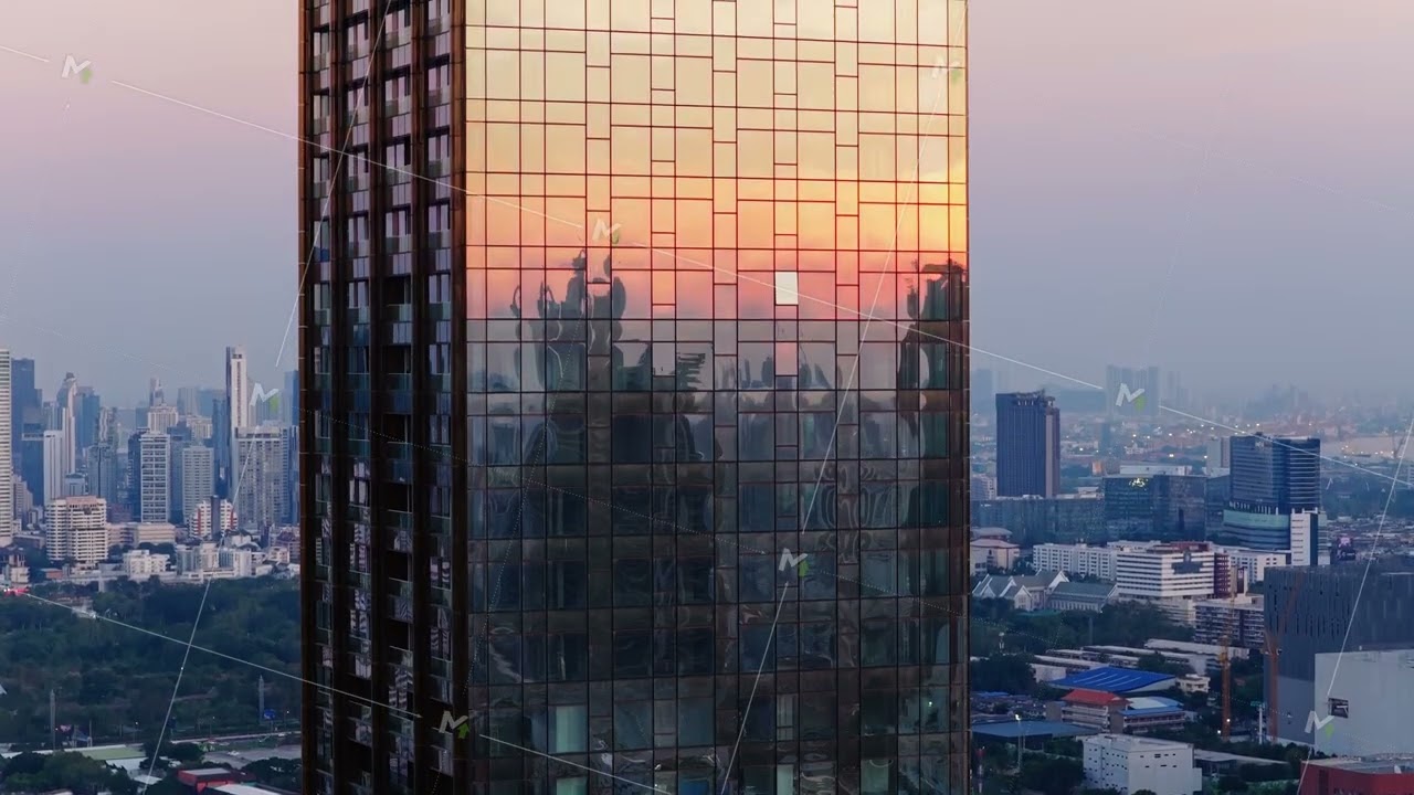 Aerial view of a modern skyscraper with a glass facade reflecting colors of the setting sun over