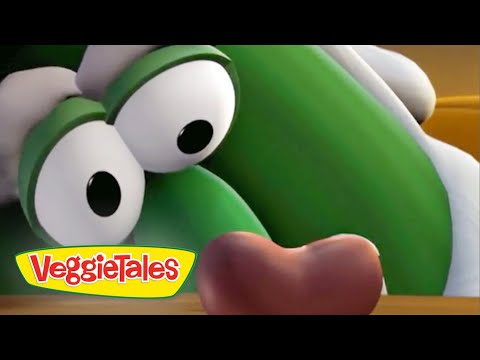 Close-up of a green VeggieTales character with large googly eyes, looking down at a brown object on a wooden surface, VeggieTales logo in the corner.