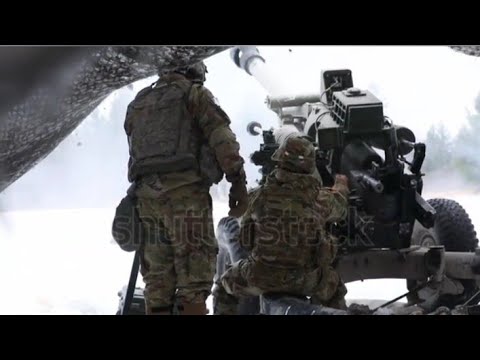 U.S. army artillery soldiers fire a massive Howitzer cannon gun on the battlefield.