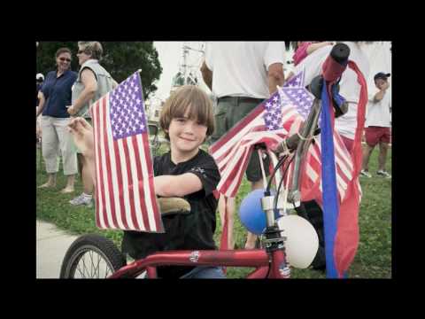 Photograph of a young boy on a bicycle decorated with American flags at a 4th of July parade.