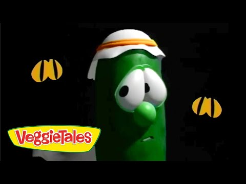 Green VeggieTales cucumber character with a white and orange headband on a black background, VeggieTales logo in the bottom-left corner.