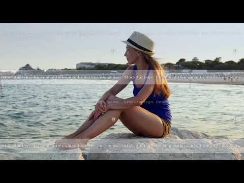 Beautiful woman sitting alone on rocky shore beach blue sky and sea background.