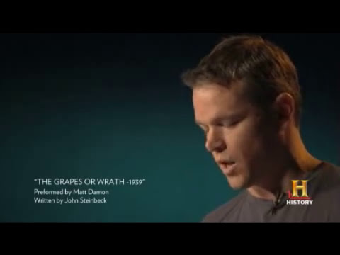 Trailer frame showing performers on a bare stage, mic stand center, audience in silhouette