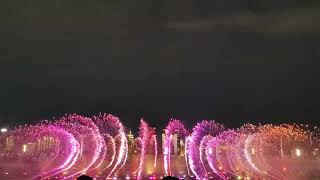 江西南昌秋水廣場夜間音樂噴泉，城市夜景與炫麗的燈光映照在水舞上。