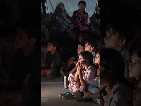 Children in Gaza gather between tents to watch cartoons